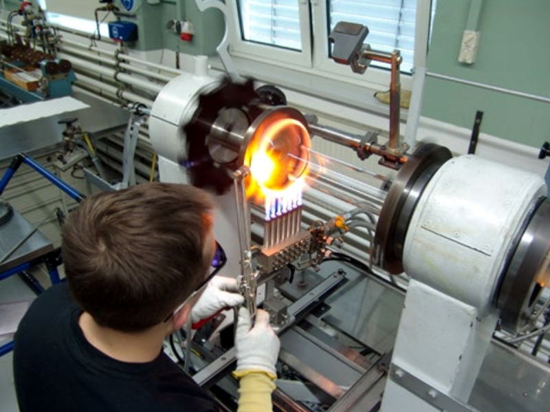 Bild von der Produktion einer Röntgenröhre in Rudolstadt 2021. Ein Arbeiter erhitzt einen Glaskolben an einer Drehbank mit einem Gasbrenner.